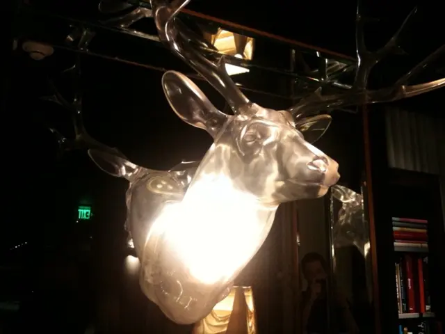 In this image there is a statue of a deer inside a building. In the right there is a book rack.