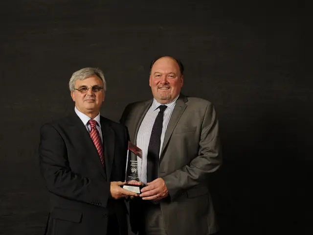 In this image there are two persons wearing suit and tie standing and holding a award in there...