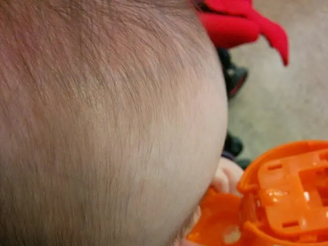 In this image I can see the baby holding the slipper and the zipper is in orange and yellow color....